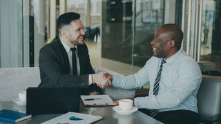 Two businessmen shaking hands across a table.